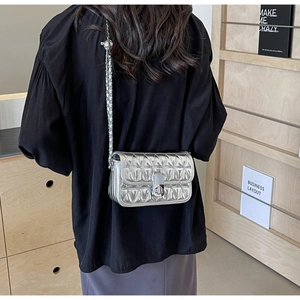 Detailed back view of a silver quilted chain bag with a metallic twist-lock on a wooden shelf