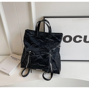 Detail of black backpack with paper-like texture, ribbon bows, and dual zippers