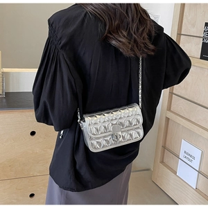 Silver quilted crossbody bag with metal chain shown on model wearing black puffed sleeve top