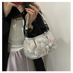 Close-up of floral embroidery detail and silver chain on vintage-style crossbody bag