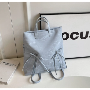 Detail of light blue crinkled fabric backpack featuring dual vertical zipper pockets and bows