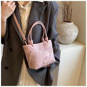 Detail of light pink bucket bag with knotted handles and metallic fashion label tag
