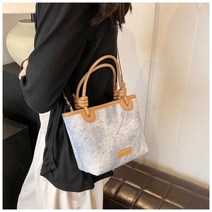 Detail of light blue denim bucket bag with brown leather trim and knot handle