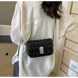 Close-up of black quilted chain bag with silver twist lock on white shirt background