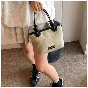 Detail of canvas bucket bag with black leather trim and fashion label on the front