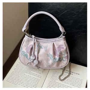 Detail of light purple floral bag with pleats and silver chain on an open book
