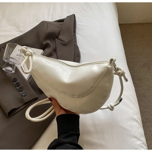 Close-up of white crescent bag with knotted rope strap and silver zipper closure