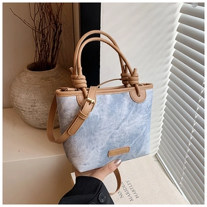 Detail of light blue denim bucket bag with brown knotted handle and leather tag