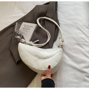 Close-up of a white crescent moon bag with knot strap detail on a dark brown suit