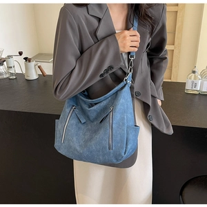 Detail of blue denim tote bag with decorative zippers and adjustable silver buckle strap