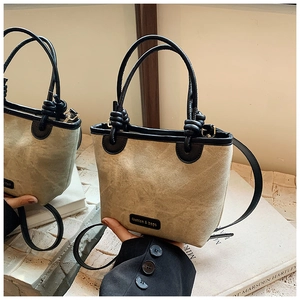 Detail of beige canvas bucket bag with black leather trim and crossbody strap