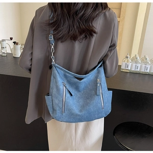 Detail of blue denim hobo bag with silver zippers shown on a shoulder in a cafe setting