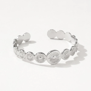 Detail of silver stainless steel bangle featuring engraved sunburst patterns on circular plates