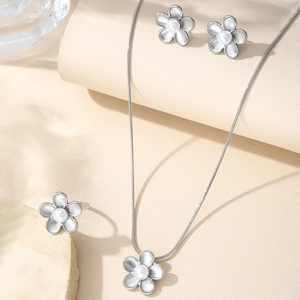 Close-up of silver flower jewelry set with necklaces, stud earrings, and ring on stone