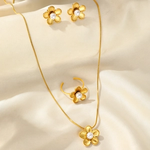 Detailed set of gold brushed flower jewelry with pearls on elegant white textured fabric