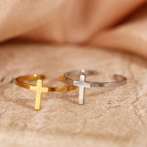 Detail view of gold and silver cross open rings on orange silk and stone surface