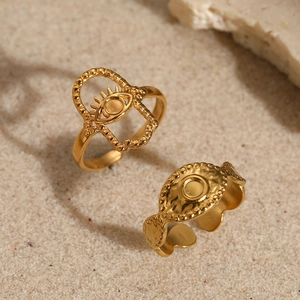 Vintage gold stainless steel rings with Hamsa Hand and hammered texture on beige sand