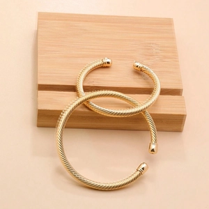 Close-up of golden cable open bracelets with twisted spiral texture on a wooden block