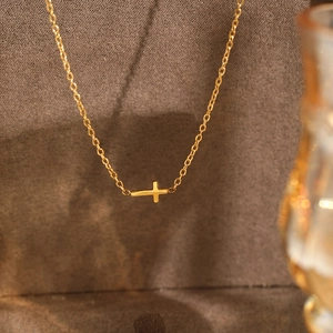 Close-up of a minimalist gold stainless steel cross pendant necklace on textured fabric