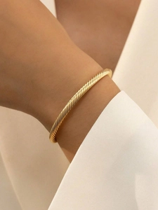 Detailed close-up of a twisted gold spiral cuff bracelet worn on a woman's wrist