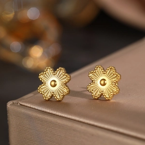 Detail view of golden four-leaf flower stud earrings with radial texture and beaded edges