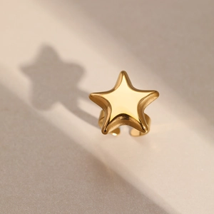 Dramatic shadow cast by a polished gold star-shaped open ring on a minimal background