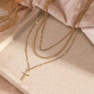 Collier multi-rangs doré avec pendentif croix présenté sur un plateau en velours