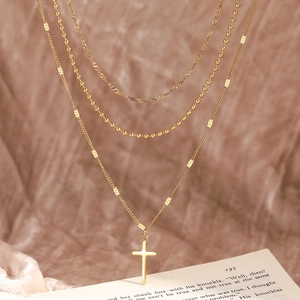 Vue détaillée du collier à trois rangs doré avec croix sur fond de livre vintage esthétique