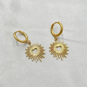 Gros plan de boucles d'oreilles créoles dorées en acier avec pendentif soleil et cœur