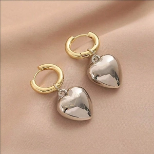 Elegant gold hoop earrings with silver heart pendants on soft pink satin fabric background