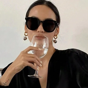 Detail of heart charm hoop earrings and black oversized sunglasses on female model