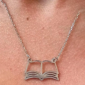 Detailed close-up of a silver stainless steel necklace with an open book hollow pendant