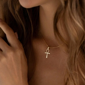 Close-up of a polished gold Ankh cross pendant necklace worn on a model's neck