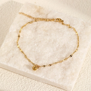 Detail of a minimalist gold beads anklet with polished spherical pendant on marble