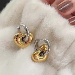 Orecchini a cuore bicolore oro e argento, stile minimalista su sfondo di peluche