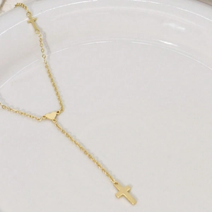 Gold Y-shaped necklace with heart connector and double cross charms on ceramic tray