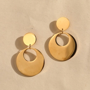 Macro detail of glossy gold circular drop earrings on textured beige paper