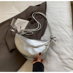 Detail showing metallic silver crescent bag texture with decorative knotted shoulder strap