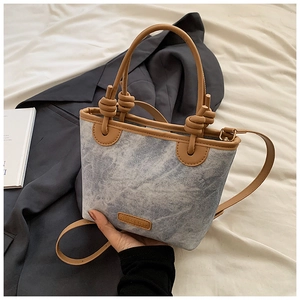 Close-up of blue denim bucket bag with brown leather trim and knotted handle detail
