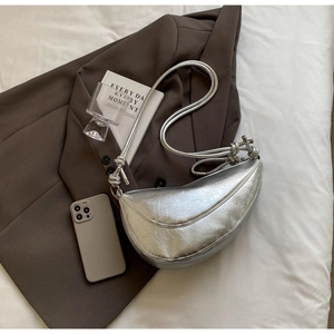 Detail of silver metallic crescent bag with knotted straps on a stylish brown blazer