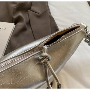 Close-up of silver textured handbag with a crackle leather finish and rope knot zipper detail