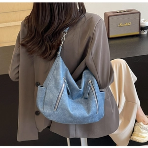 Detail of blue denim tote bag featuring side pockets and polished metal shoulder strap buckles