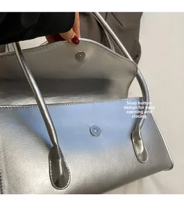 Detail of silver textured underarm bag featuring secure magnetic snap closure design