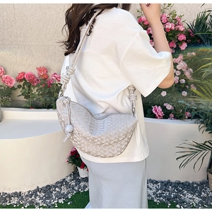 Détail du sac hobo tissé beige avec bandoulière nouée dans un décor de jardin