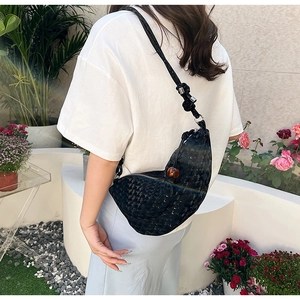 Sac bandoulière demi-lune noir chic avec perle d'ambre porté dans un jardin fleuri