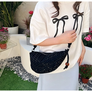 Détail du sac croissant tissé noir avec une longue bandoulière et une perle ambre