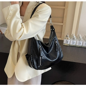 Detail of a vintage black faux leather tote bag with silver zippers on a model