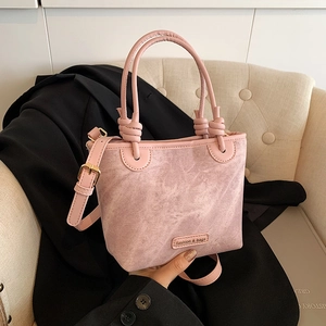 Pink fashion bucket bag with knot handles and crossbody strap on a beige sofa