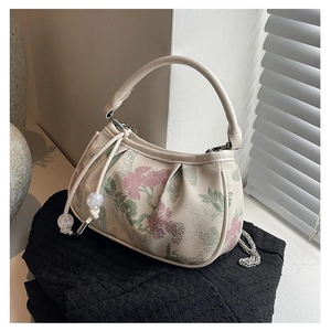 Detail of floral embroidery on a white handbag with drawstring and metal chain