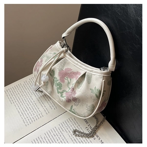 Detail of floral embroidery on small square bag with textured pleats and chain strap